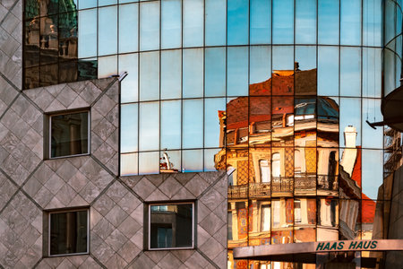 A modern building with several windows reflecting an old building at sunsetの写真素材