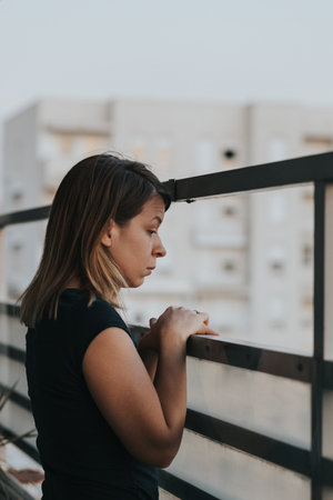 A thoughtful young Caucasian woman looking outside from her apartment balcony in Belgrade, Serbiaの写真素材