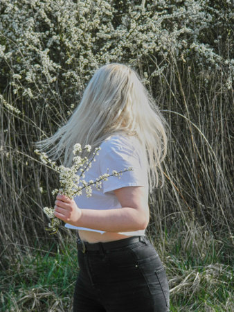 A vertical shot of a Caucasian young woman with long white hair holding flowers in a fieldの写真素材