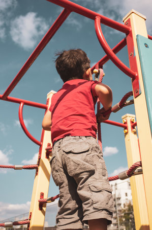 A closeup of a Caucasian boy with a red t-shirt climbing the stairs in an outdoor playground