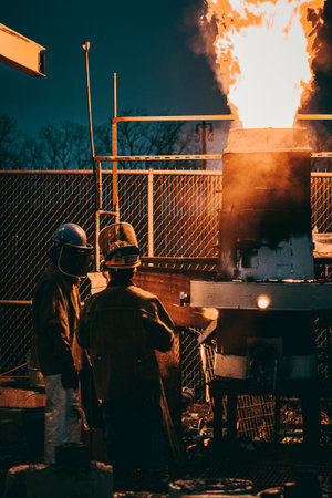 A vertical shot of adult industrial workers in uniforms melting metal in a factoryの写真素材