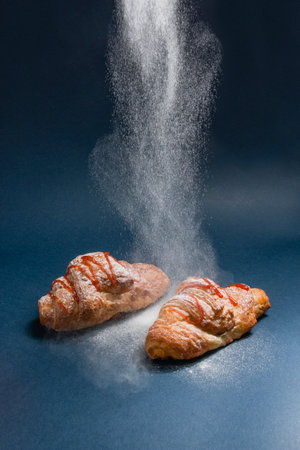 A portrait of croissants being dusted with powdered sugar on a black backgroundの写真素材