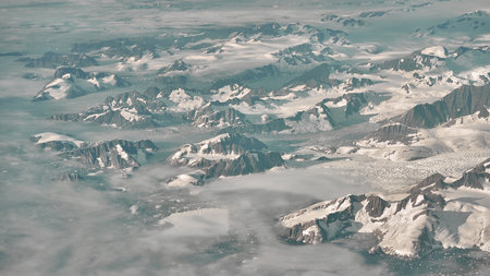 A magnificent aerial shot of high, foggy mountains partly covered in snow and iceの写真素材