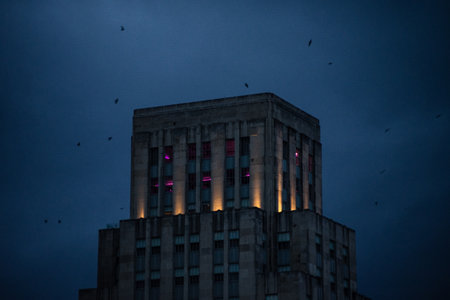 A closeup of a building top with lights and pink neon lights inside with birds flying above in...