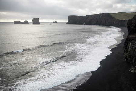 A scenic view of kirkjufjara beach and dyrholaey peninsula against cloudy sky in south Iceland