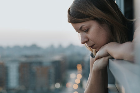 A thoughtful young Caucasian woman looking outside from her apartment balcony in Belgrade, Serbiaの写真素材