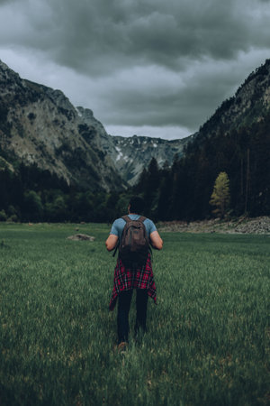 A young hiker with a backpack in a field surrounded by rocky hills under a stormy skyの写真素材