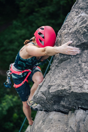 A climber climbing a rock. Adventure sport activity, adrenaline. Girl climbing with a rope, helmet and other climbing equipment. Sport climbing.の写真素材