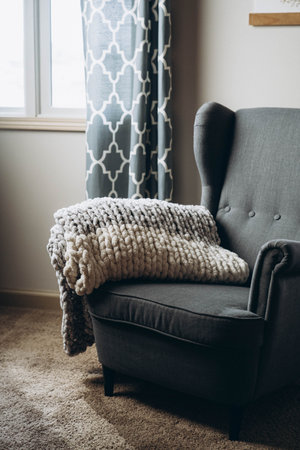 A vertical shot of the soft custom made chunky blanket on an armchair in the house