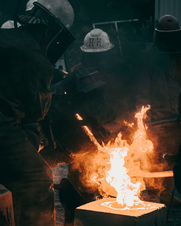 A vertical shot of adult industrial workers in uniforms melting metal in a factory
