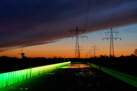 A scenic shot of electricity towers located behind a small water stream during the sunsetの写真素材