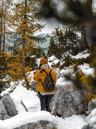 A Caucasian female hiker wearing winter clothes and a backpack walking on a snowy path in the forestの写真素材