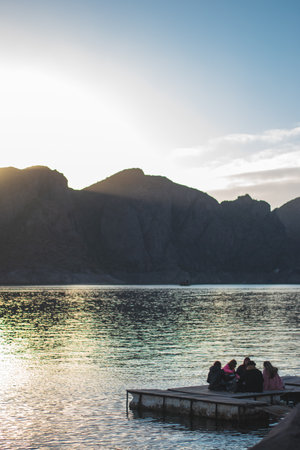 A vertical shot of the group of people sitting on the deck near the lake.の写真素材