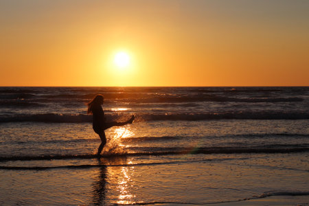 A silhouette of a happy female splashing water on a coastline at sunset