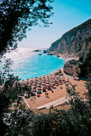 A vertical shot of umbrellas on a beach surrounded by cliffs and sea in Budva, Montenegro