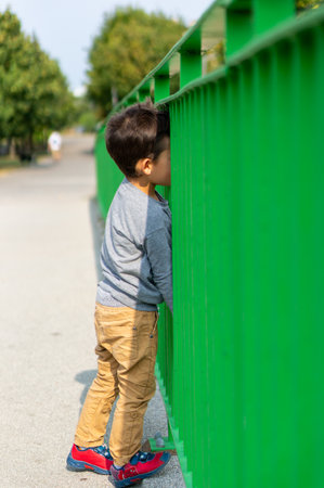 A vertical shot of a boy standing behind a green metal barrierの写真素材