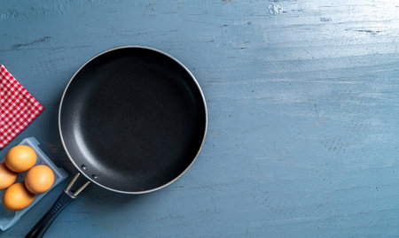 A top view of a black frying pan and eggs on a blue wooden tableの写真素材