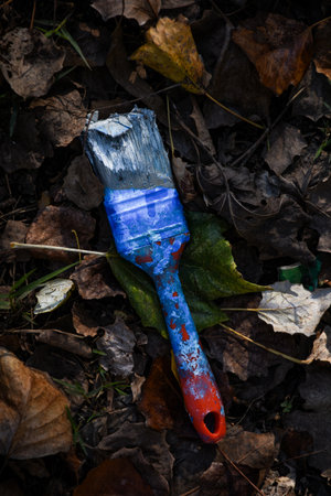 A vertical shot of a dirty big paintbrush on a forest floor