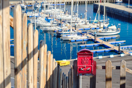 Red vintage mailbox with a wooden fence in front of the small harbor of Puerto de la Estaca. Idyllic...