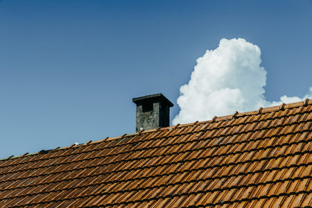 A low angle shot o the roof and the chimney under the sky with puffy cloudsの写真素材