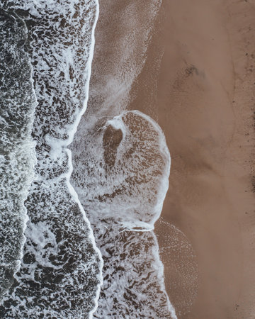 A top view of foam waves hitting a sandy seashore