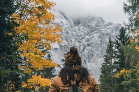 Rear view of female hiker walking on path leading to amazing mountains. Autumn and fall colors of...