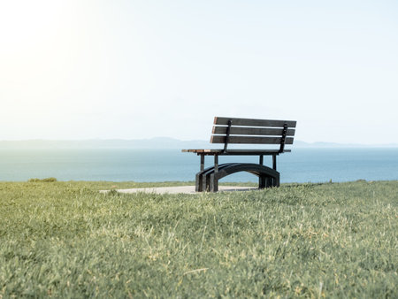 View of Bench on green grass, water and sky sceneryの写真素材