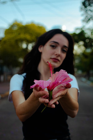 A vertical shot of a young beautiful female posing with a pink Hibiscus flower