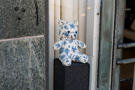 A blue and white teddy bear sitting and looking out of the window
