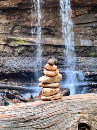 A vertical shot of a stack of stones on a log by the waterfall in a forest in Pittsburghの写真素材