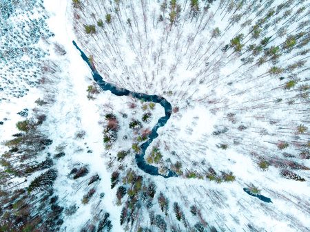 An aerial shot of river flowing through snowy forestの写真素材
