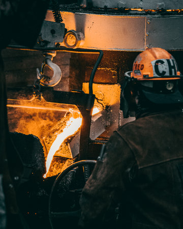 A vertical shot of an adult industrial worker in uniforms melting metal in a factoryの写真素材