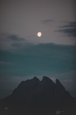 A vertical shot of rocky mount silhouette at night under a full moon skyの写真素材