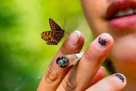 A closeup shot of a hand holding a cigarette with a butterfly on itの写真素材