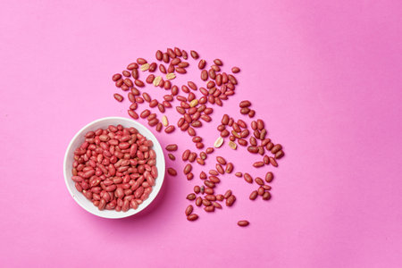 A top view shot of a bowl of peanuts on a pink background