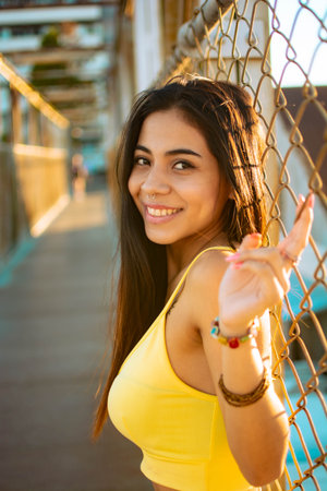 A young Hispanic woman leaning on the fence grid during a sunny dayの写真素材