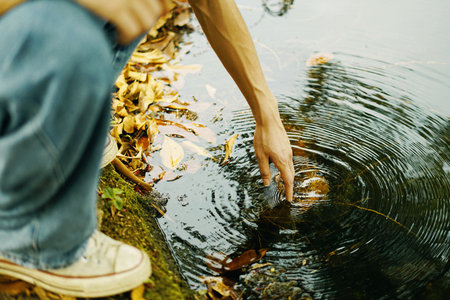 A boy leaning down to touch the water, artsy aesthetic