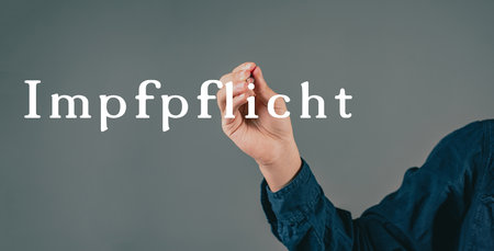 Mandatory vaccination is standing in german language on a grey background, hand with a pen is...