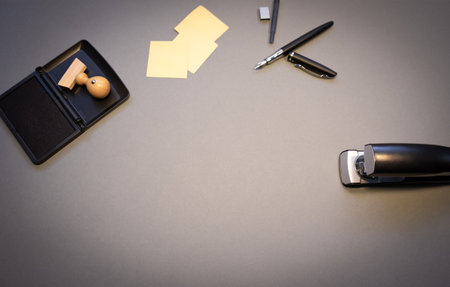 A top view of a wooden stamp with ink, metal stapler, sticky notes and markers isolated on a gray...
