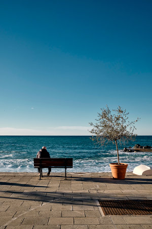 a beautiful shot of a man sitting on a bench looking to the sea in Camogli fishing village