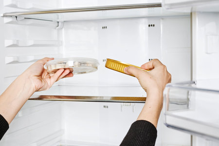 A closeup shot of female hands putting food in containers to the empty refrigeratorの写真素材