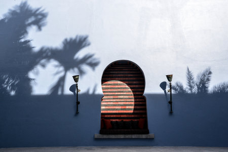 A blue wall with the shadows of trees and a place for sitting and lanterns