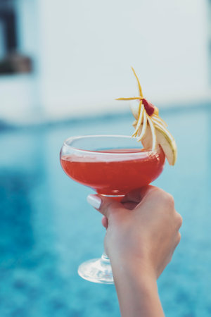 A closeup of a female hand holding a cocktail in a poolの写真素材