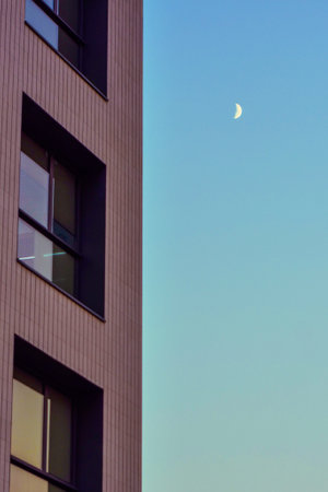 A vertical shot of a small shining moon near a building facade