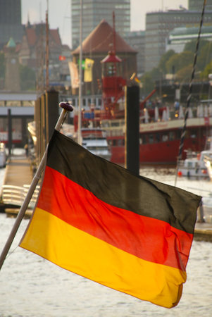 A vertical closeup shot of the German flag waving against a harbor and buildingsの写真素材