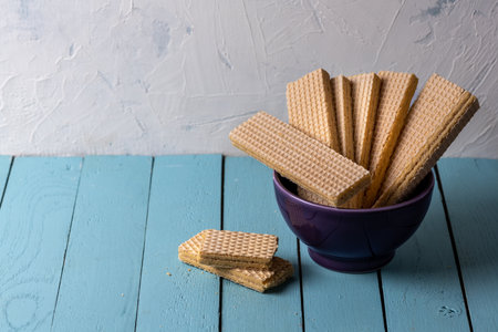 A photo of wafers in a purple bowl and wafers on a blue wooden table against a white wallの写真素材