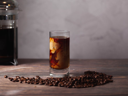 a cup of cold brew coffee surrounded by coffee beans on a woody table.