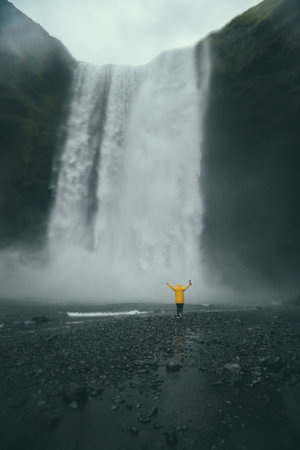 A vertical shot of a person enjoying the view of a waterfall in Iceland