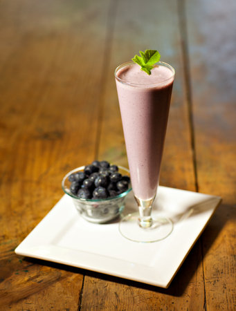 A serving of a glass of smoothie with mint on top and blueberries on a plate on a wooden tableの写真素材