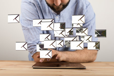 A 3D rendering of silver email icons floating in the air with a man looking at a tablet under themの写真素材